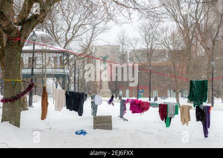 Clothing hanging on a rope in a park. The clothing was left for homeless and other people in need. Ground covered with snow, and snow falling. Stock Photo