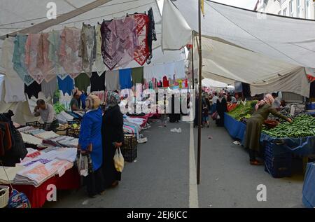 Everyday market in Istanbul with people shopping for bargains. Headscarves one side with fruit and vegetables on the other. June 2018 Stock Photo