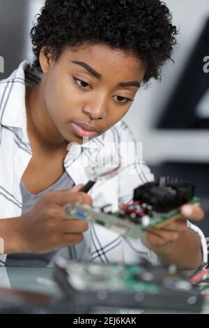female computer technician looking at component through magnifying glass Stock Photo