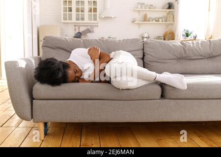 Depressed unhappy Black woman lying on couch at home, crying, suffering from divorce or break up.  Stock Photo