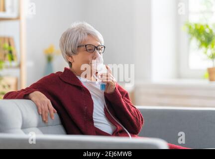 Elderly woman using inhaler for asthma and respiratory diseases at home. Stock Photo