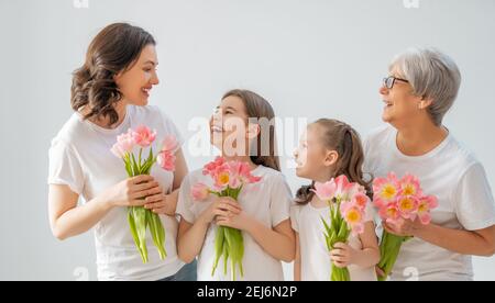 Happy women's day! Children daughters are congratulating mom and grandma giving them flowers tulips.Granny, mum and girls smiling on light grey backgr Stock Photo