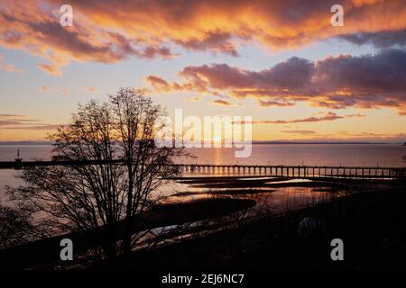 Spectacular sunset over White Rock's silhouetted pier and beach.   Colorful clouds overhead are reflected in shallow tide pools. Stock Photo