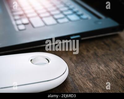 Close up modern white wireless mouse beside black laptop computer on wooden desk. Stock Photo