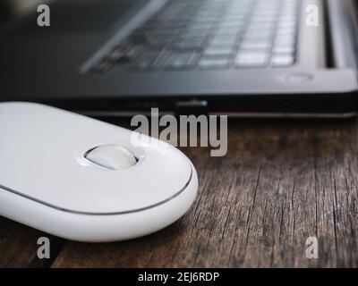 Close up modern white wireless mouse beside black laptop computer on wooden desk. Stock Photo