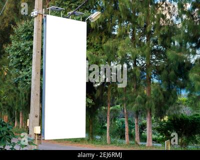 Empty white blank banner on electric pole for advertising beside the road near the tree and green garden. Billboard mockup or flag street hanging on t Stock Photo