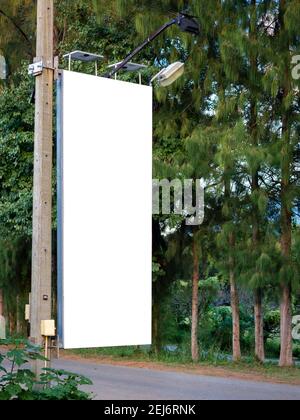 Empty white blank banner on electric pole for advertising beside the road near the tree and green garden. Billboard mockup or flag street hanging on t Stock Photo