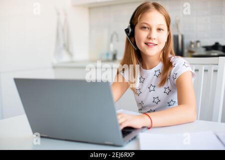 Female student at home in front of a laptop monitor. She does teacher-led lessons online. She looking at camera and smiling. Stock Photo