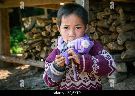 Closeup of a small boy holding his purple toy outside his house in the village with firewood in background. Stock Photo