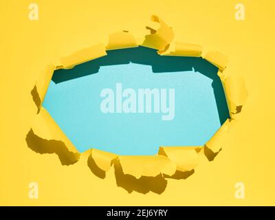 Torn bright yellow and blue empty paper background. Copy space. Yellow paper with oval hole with blank blue background inside for message, design or text. Hard light, sunny day. Stock Photo