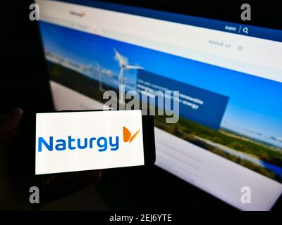 Person holding cellphone with business logo of Spanish energy company Naturgy Energy Group SA on screen in front of website. Focus on phone display. Stock Photo