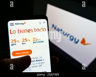 Person holding smartphone with website of Spanish energy company Naturgy Energy Group SA on screen with logo. Focus on center-left of phone display. Stock Photo