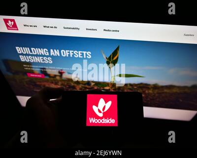 Person holding mobile phone with logo of Australian oil company Woodside Petroleum Ltd on screen in front of webpage. Focus on cellphone display. Stock Photo