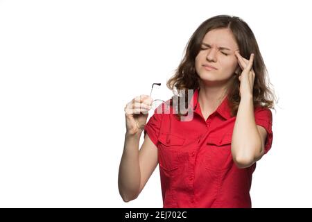 Beautiful young girl in a red shirt on a white background who has sore eyes and a head from glasses Stock Photo