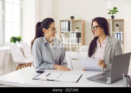 Happy client and bank manager sitting at desk, looking at each other and smiling Stock Photo