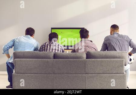 Back view of young men sitting on comfortable sofa and watching football match on TV Stock Photo