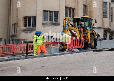 Repair works on urban sidewalk, digger and workmen in high visibility clothing working in street Stock Photo