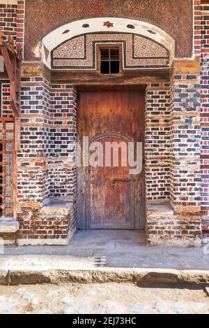 Wooden grunge decorated arched entrance gate with inner small wooden door on wall with black and red bricks with white seam Stock Photo