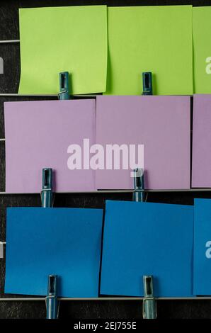 The paper sticky notes hanging from clothespins. Set of multicolored blank square stickers on black background. No people. Stock Photo