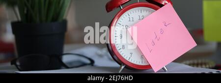 Red alarm clock standing on table near flowerpot in office closeup Stock Photo