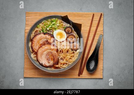 A Shoyu Ramen in gray bowl on concrete table top. Japanese cuisine meat noodle soup with chashu pork. Asian food. Top view Stock Photo