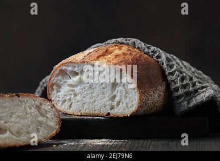 freshly baked bread covered with grey towel on black wooden cutting board Stock Photo