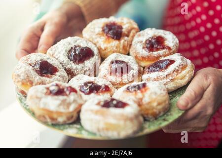 Plate full of jam-filled donuts with sugar coating held in the hands of an older woman. Stock Photo
