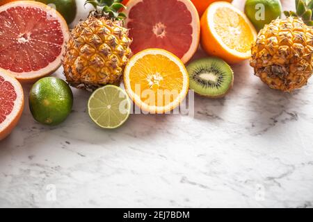 Various citruses such as oranges, limes, grapefruits, as well as pineapples on a marble surface. Stock Photo