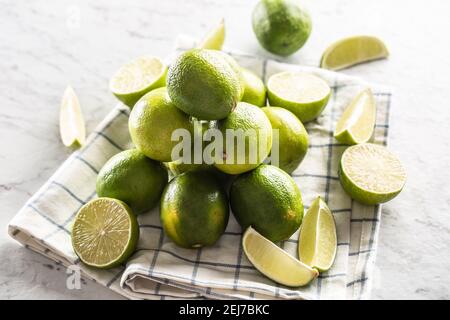 Cut and whole limes on a kitchen towel and a marble surface. Stock Photo