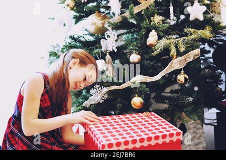 European child (girl, 8-9 years old) with Christmas presents, opening a big red box. Filter applied Stock Photo