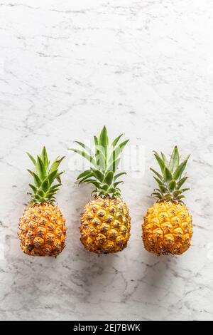 Three fresh whole pineapples with leaves on a marble surface. Stock Photo