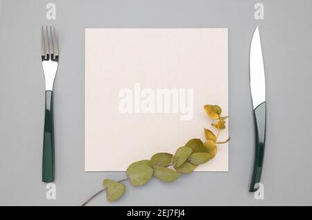 Mockup menu, recipe or cookbook. knife, fork, square paper mockup decorated with gold eucalyptus branch on a neutral table. Stock Photo