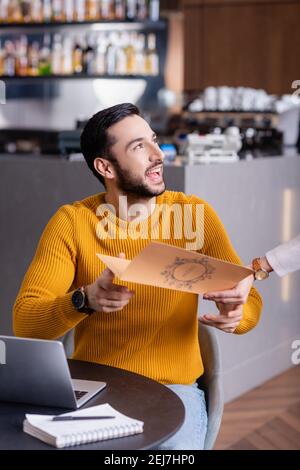 excited arabian freelancer taking menu card from waitress in restaurant Stock Photo