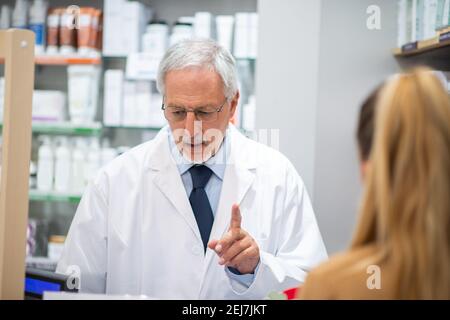 Senior pharmacist serving a female customer in his pharmacy Stock Photo