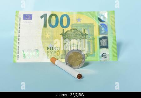 Cigarettes and money on blue background. Euro banknotes and coins, cost of smoking, cigarette price concept. Selective focus Stock Photo