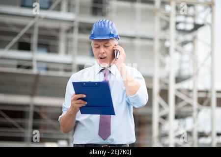 Architect site manager talking on the cellphone in front of construction site Stock Photo