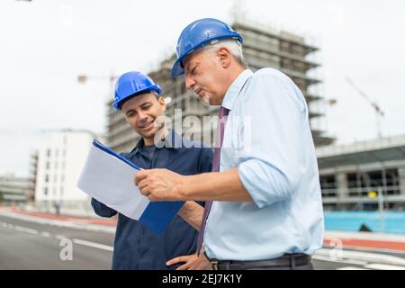 Two architect developers reviewing building plans in front of their construction site Stock Photo