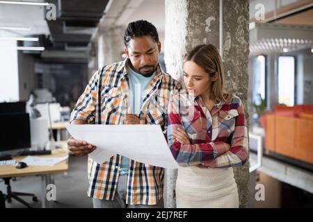 Young architect colleagues are analyzing blueprints while working on a new project Stock Photo