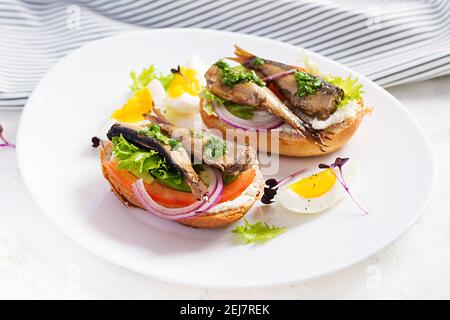 Sandwich - smorrebrod with sprats, avocado, tomatoes, eggs and cream cheese on white plate. Danish cuisine.  Eco friendly concept. Stock Photo