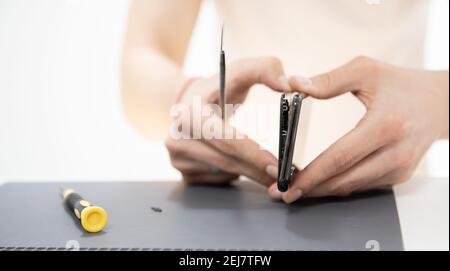 Master disassembles modern mobile phone, repairs and replaces battery, broken screen. Stock Photo
