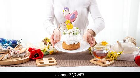 Women's hands are holding a festive Easter cake, decorated with flowers and bright details. The concept of preparing for the Easter holiday. Stock Photo