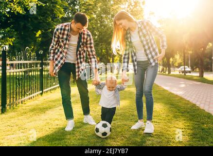 Enjoy your time together. Young happy family, father and mother, hold hands of their little son, walk in the park together with a ball Stock Photo