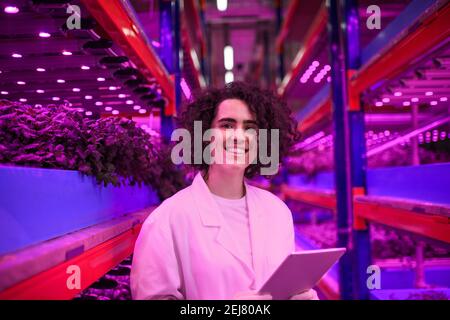 Worker with tablet looking at camera on aquaponic farm, sustainable business and artificial lighting. Stock Photo