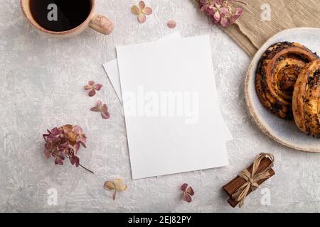 White paper invitation card, mockup with hydrangea flowers, bun, cup of coffee, linen textile, cinnamon on gray concrete background. Blank, flat lay, Stock Photo