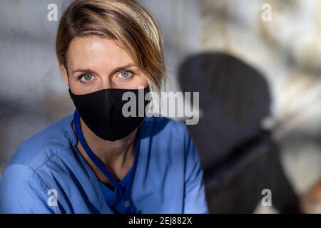 Tired woman caregiver, nurse or healthcare worker sitting and looking at camera outdoors, taking a break. Stock Photo