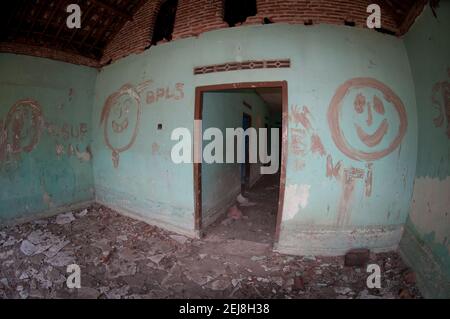 Abandoned house with graffiti on turquoise walls with dried mud on floor following flooding by mud lake environmental disaster which developed after d Stock Photo
