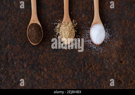 Brown, muscovado, and regular sugar in wooden spoons on a dark backdrop. Stock Photo