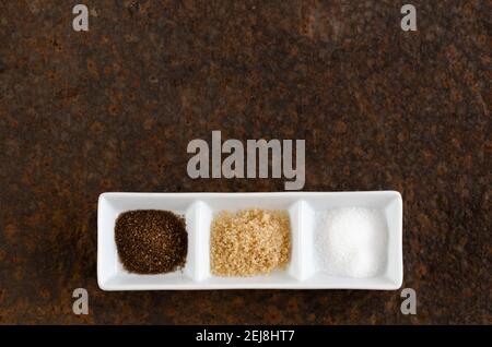 Brown, muscovado, and regular sugar in white squared bowls on a dark backdrop. Stock Photo