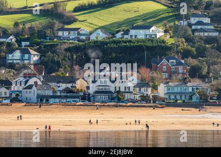 Instow, North Devon, England. Monday 22nd February 2021. UK Weather. After a week of grey skies in North Devon, a brighter start to the new week tempts people out for a 'socially distanced' walk on the beach for their daily exercise at the picturesque coastal village of Instow. Credit: Terry Mathews/Alamy Live News Stock Photo