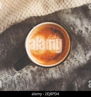 On top of the gray warm knit sweaters is a black mug with a fragrant strong coffee with cinnamon, illuminated by the morning light. A invigorating dri Stock Photo